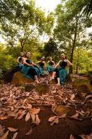 eine gruppe asiatischer frauen macht urlaub im wald, während sie einen grünen rock tragen und auf einem felsen sitzen foto