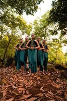 eine Weiteinstellung einer asiatischen Frau, die zusammen im Wald steht, während sie ein grünes Tanzkostüm mit abgestorbenen Blättern trägt foto