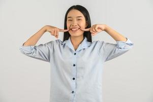 Porträt einer glücklichen jungen asiatischen Frau im blauen Hemd, die mit dem Finger auf die Wange lächelt, isoliert auf weißem Hintergrund foto