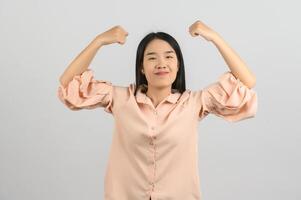 Porträt einer jungen asiatischen Frau im rosafarbenen Hemd, die eine starke Geste macht, die auf weißem Hintergrund isoliert ist foto