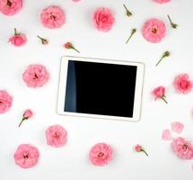 Weißes elektronisches Tablet mit einem leeren schwarzen Bildschirm und blühenden Knospen einer rosa Rose auf weißem Hintergrund foto