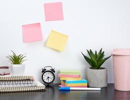 Stapel von Spiralheften und farbigen Aufklebern, neben einem Keramiktopf mit einer Blume auf einem schwarzen Tisch foto