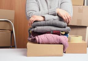 frau in einem grauen pullover packt kleidung in eine kiste, das konzept der hilfe und freiwilligenarbeit, bewegt sich foto