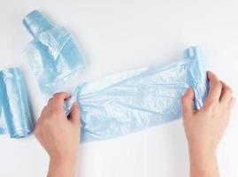 weibliche hand wickelt eine blaue plastiktüte für müll ab foto