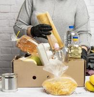 frau in einem grauen pullover verpackt lebensmittel in einem pappkarton, das konzept der hilfe und des freiwilligendienstes foto