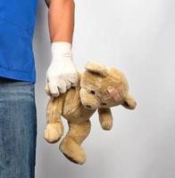 Arzt in blauer Uniform und weißen Latexhandschuhen mit braunem Teddybär foto