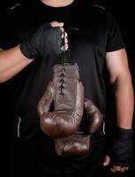 Sportler in schwarzer Kleidung hält sehr alte braune Boxhandschuhe aus Vintage-Leder foto