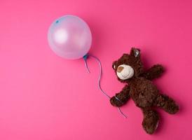 kleiner brauner Teddybär, der einen blauen aufgeblasenen Ballon hält foto