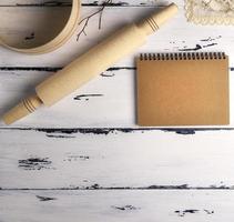 Öffnen Sie ein leeres Notizbuch mit braunen Seiten und einem hölzernen Nudelholz mit einem runden Holzsieb foto