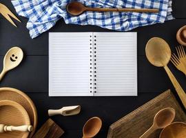 Öffnen Sie ein leeres Notizbuch aus Papier mit weißen Blättern in einer Linie auf einer Feder inmitten von Küchenartikeln aus Holz foto