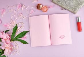 offenes notizbuch mit leeren rosa seiten, einem blumenstrauß aus pfingstrosen, rotem lippenstift foto