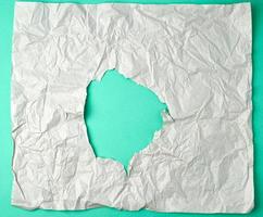 graues, zerknittertes Blatt Papier mit einem Loch, grüne Unterlage foto