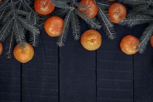 zweig aß mit reifen mandarinen auf einer schwarzen holzoberfläche, draufsicht foto