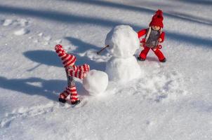 zwei kleine Holzmänner in der Szene, in der ein Schneemann im reinen weißen Schnee gebaut wird foto