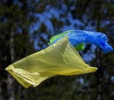 Zwei Müllsäcke aus Polyethylen fliegen vor dem Hintergrund eines Kiefernwaldes in der Luft foto