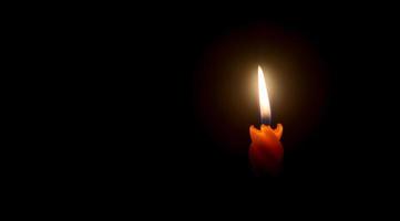 Einzelne brennende Kerzenflamme oder Licht, das auf einer spiralförmigen orangefarbenen Kerze vor wenig Wind auf schwarzem oder dunklem Hintergrund auf dem Tisch in der Kirche zu Weihnachten, Beerdigung oder Gedenkfeier leuchtet foto