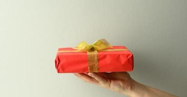 weibliche Hand hält eine rote Geschenkbox auf grauem Hintergrund, alles Gute zum Geburtstag Konzept foto