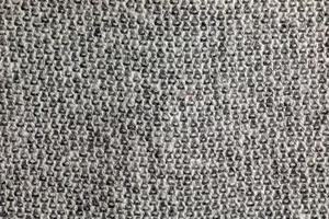 Nahaufnahme des grauen gestrickten Teppichs. Textilstruktur auf grauem Hintergrund. detaillierter hintergrund aus warmem garn. natürlicher Wollstoff, Pulloverfragment. foto
