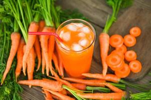 Karottensaft auf Holztischhintergrund, frische und süße Karottenscheiben zum Kochen von Obst und Gemüse für das Gesundheitskonzept, frischer Karottensaft auf Glas mit Eis im Sommer foto