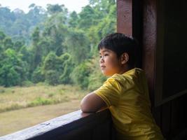 Junge, der aus dem Fenster blickt und den grünen Wald betrachtet foto