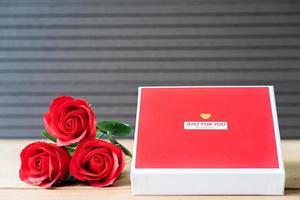 rote Rosen und herzförmige Schachtel auf Holzhintergrund foto