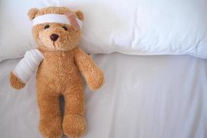 teddybär liegt krank im bett mit einem stirnband und einem tuch bedeckt foto