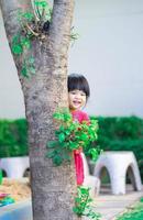kleines Mädchen, das sich hinter den Baum im Park schleicht foto
