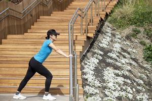 Frau läuft in einem blauen T-Shirt, das Dehnübungen neben einer Holztreppe macht. Konzept für ein gesundes Leben. foto