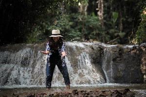 junge Frau, die Spaß unter einem Wasserfall im Wald hat