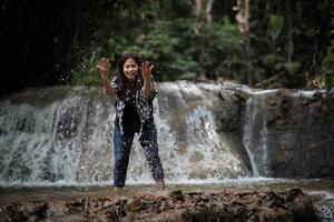 junge Frau, die Spaß unter einem Wasserfall im Wald hat foto