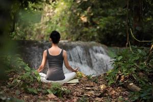junge Frau in einer Yoga-Pose, die nahe einem Wasserfall sitzt foto
