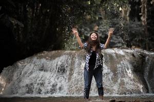junge Frau, die Spaß unter einem Wasserfall im Wald hat foto