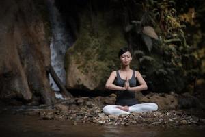 junge Frau in einer Yoga-Pose, die nahe einem Wasserfall sitzt foto