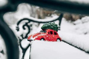 Spielzeug rotes Auto schleppt einen Weihnachtsbaum auf dem schneebedeckten Sitz foto