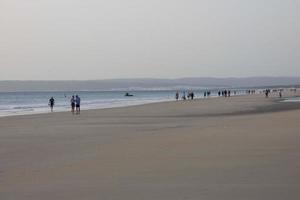 Einsamer Strand mit Menschen, die auf dem Sand am Rand der Meereswellen spazieren gehen foto