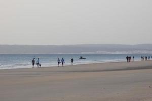 Einsamer Strand mit Menschen, die auf dem Sand am Rand der Meereswellen spazieren gehen foto