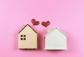 Flache Lage von zwei hölzernen Modellhäusern mit roten Glitzerherzen auf rosa Hintergrund. Traumhaus, Heimat der Liebe, starke Beziehung, Nachbarhäuser, Valentinstag. foto