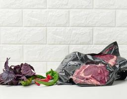vakuumverpacktes rohes Rindfleisch, Chilischoten, ein Bund Basilikum auf einem Abelom-Tisch foto