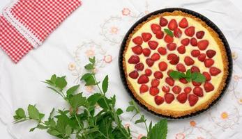 gebackene runde Torte mit Erdbeeren und zarter Milchcreme auf weißem Tischhintergrund foto