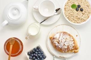 rohes hafermehl in weißer keramikplatte, blaubeere, honig auf weißem tisch, frühstück. Ansicht von oben foto
