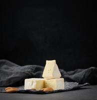 Runder Brie-Käse auf schwarzem, zerknittertem Papier, Holztisch foto