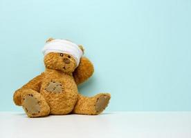 Kinderspielzeug-Teddybär sitzt mit bandagiertem Kopf. Kindheitstrauma-Konzept foto