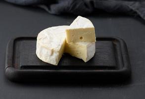 runder Brie-Käse auf braunem Holzschneidebrett, schwarzer Hintergrund foto