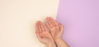 Zwei weibliche Hände falteten sich von Handfläche zu Handfläche auf einem beige-violetten Hintergrund foto