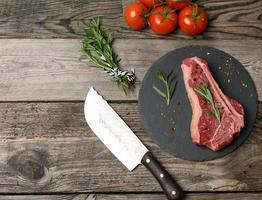 frisches Stück Rindfleisch, Roastbeefsteak auf einem schwarzen Brett mit Gewürzen foto