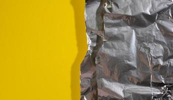 zerknittertes Blatt aus grauer Folie zum Verpacken von Produkten mit zerrissenen Kanten auf gelbem Hintergrund foto
