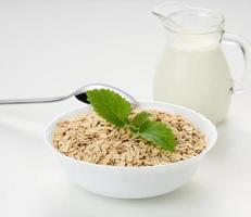 Milch und weiße Schüssel mit trockenen Haferflocken auf weißem Hintergrund, Frühstück foto