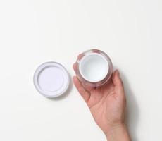 weibliche hand, die leeres weißes plastikglas hält. Verpackung für Creme, Gel, Serum foto