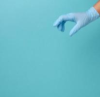 Die Hand des Arztes in einem blauen medizinischen Handschuh hält ein Objekt auf blauem Hintergrund foto