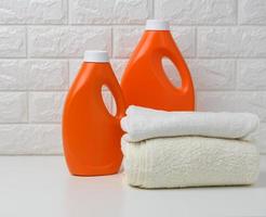 Orangefarbene Plastikflasche mit flüssigem Waschpulver und gefalteten Handtüchern auf einem weißen Regal foto